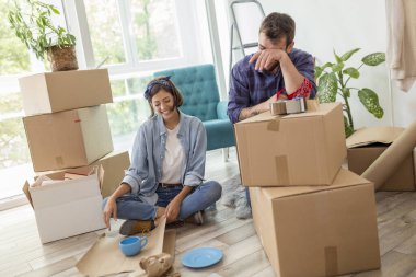 Aşık bir çift karton kutulara bir şeyler paketliyor, taşınmaya hazırlanıyor - erkek kutuları ambalaj makinesiyle bantlarken kadın kırılgan şeyleri kağıda sarıyor.