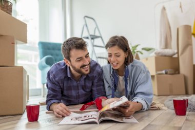 Birbirine aşık bir çift yeni evlerinin zemininde uzanıyor, ev dekorasyonu dergilerini karıştırıyor ve kahve içiyor.