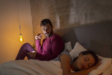 Kız arkadaşı geceleri yatakta uyurken akıllı bir telefona mesaj yazan bir adam. Uykusuzluk ve aldatma kavramı.