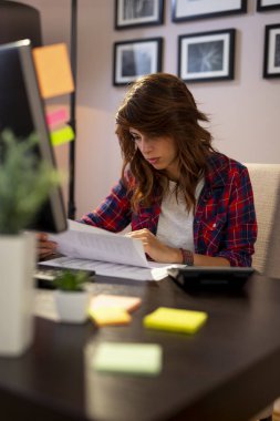 Evrakları inceleyen, geç saatlere kadar çalışan genç bir kadın.