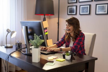 Ev ofisinde çalışan, klavyeyle yazı yazan genç bir kadın bilişim uzmanı.