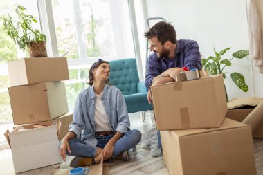 Aşık bir çift karton kutulara bir şeyler paketliyor, taşınmaya hazırlanıyor - erkek kutuları ambalaj makinesiyle bantlarken kadın kırılgan şeyleri kağıda sarıyor.