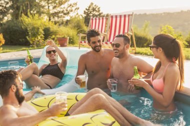 Havuz başında bir yaz partisinde, bira içip havuzda eğlenen bir grup arkadaş.