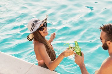 Havuz başında bir yaz partisinde aşık bir çift havuz kenarında suyun içinde durup kadeh kaldırıyor.