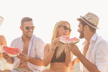 Havuz başında bir yaz partisinde bir grup arkadaş, yüzme havuzunun kenarında oturmuş, soğuk karpuz dilimleri yiyor ve eğleniyorlar.