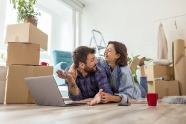 Birbirine aşık güzel genç bir çift birlikte yaşıyor, dizüstü bilgisayarla internette sörf yapıyor, internette daire dekorasyonu fikirleri arıyor.