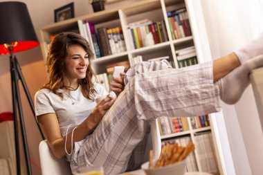 Güzel, genç bir kadın pencerenin yanında oturuyor, kahvaltı yapıyor, kahve içiyor, elinde akıllı bir telefon tutuyor ve bir mesaj yazıyor.