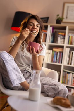 Kahvaltıda süt ve mısır gevreği yiyen güzel genç bir kadın.