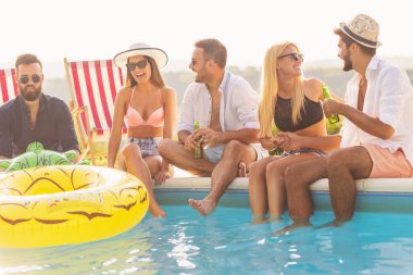 Havuz başında bir yaz partisinde bir grup arkadaş, yüzme havuzunun kenarında bacakları suyun içinde, bira içip eğleniyorlar.