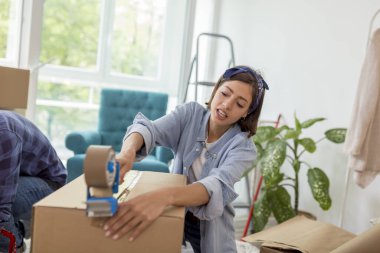 Güzel genç bir kadın ambalaj makinesi kullanıyor, karton kutuları kaydediyor, taşınmaya hazırlanıyor, taşınırken eşyalar paketleniyor.