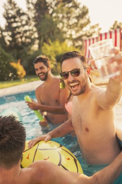 Havuz başında bir yaz partisinde bir grup arkadaş, yüzme havuzunda eğleniyorlar, kokteyl ve bira içiyorlar ve kadeh kaldırıyorlar.