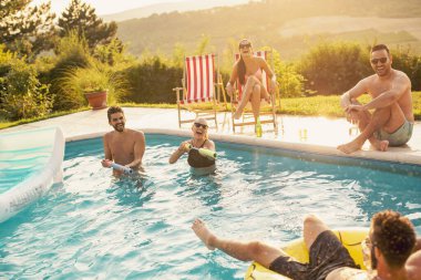 Havuz başında bir yaz partisinde bir grup arkadaş yüzme havuzunda eğleniyor, bira içiyor ve su sıçratıyor.