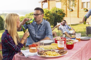 Arkadaşlar arka bahçede barbekü partisi veriyor, bira içiyor, et pişiriyor ve güneşli bir yaz gününde eğleniyorlar.