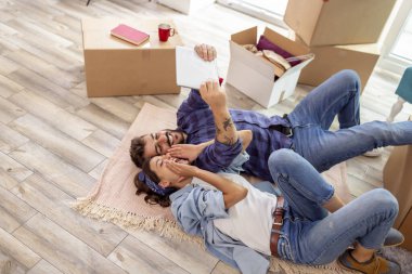 Birbirine aşık çiftlerin yeni evlerinin zemininde yatıp tablet bilgisayar kullanarak görüntülerini izliyorlar.