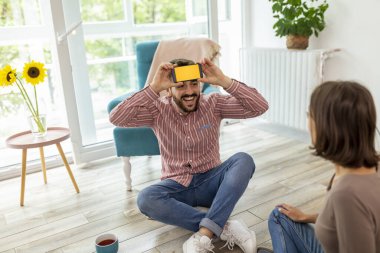 Çift evde sessiz sinema oynayarak eğleniyor, akıllı bir telefon uygulamasından kelimeleri izah ediyor ve tahmin ediyor.