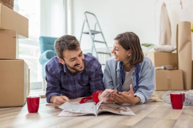 Birbirine aşık bir çift yeni evlerinin zemininde uzanıyor, iç tasarım fikirleri arıyor, ev dekorasyonu dergilerini karıştırıyor ve kahve içiyor.