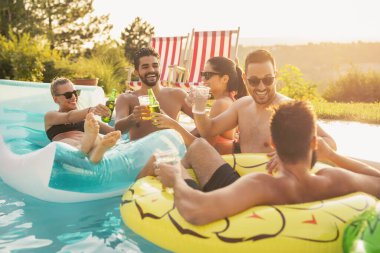 Havuz başında bir yaz partisinde bir grup arkadaş, yüzme havuzunda eğleniyorlar, kokteyl ve bira içiyorlar ve kadeh kaldırıyorlar.