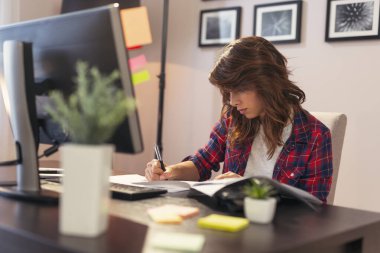 Ev ofisinde çalışan genç bir kadın, kontrat imzalıyor.