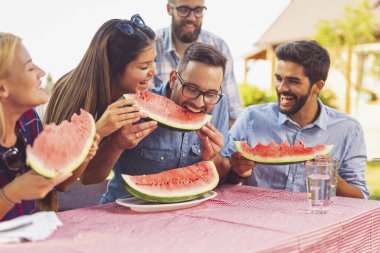 Bir grup arkadaş dışarıda öğle yemeği yiyor, taze karpuz dilimleri yiyor ve eğleniyorlar.