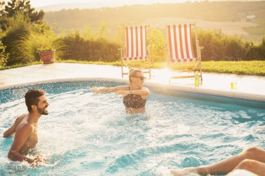 Havuz başında bir yaz partisinde bir grup arkadaş, yüzme havuzunda eğleniyorlar, su sıçratıyorlar.