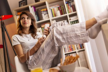 Güzel, genç bir kadın pencerenin yanında oturuyor, kahvaltı yapıyor, kahve içiyor, elinde akıllı bir telefon tutuyor ve bir mesaj yazıyor.