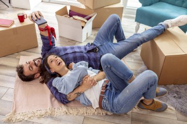 Birbirine aşık çiftlerin yeni evlerinin zemininde yatıp selfie çektikleri yüksek açılı bir manzara.