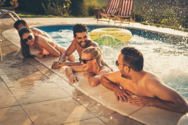 Havuz başında bir yaz partisinde bir grup arkadaş, yüzme havuzunda eğleniyorlar, su sıçratıyorlar ve gülüyorlar.