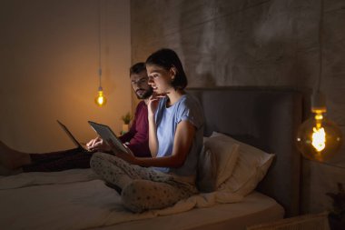 Güzel genç çift geceleri yan yana oturup laptopta ve tablet bilgisayarlarda geç saatlere kadar çalışıyorlar.