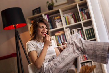 Güzel bir genç bayan hafta sonu sabahının tadını çıkarıyor, kahvaltı yapıyor ve taze çilek yiyor.