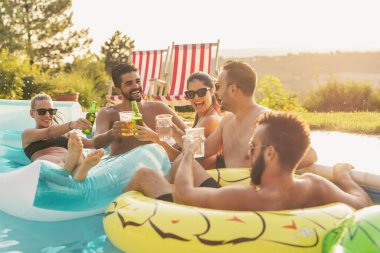 Havuz başında bir yaz partisinde bir grup arkadaş, yüzme havuzunda eğleniyorlar, kokteyl ve bira içiyorlar ve kadeh kaldırıyorlar.