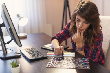 Ev ofisinde çalışan kadın grafik tasarımcısı, renk paletinden bir renk seçer