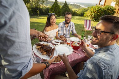 Bir grup arkadaş dışarıda barbekü yapıyor, ızgara et yiyor, bira içiyor ve eğleniyorlar. Ete ve tabağa odaklan.