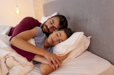 Birbirine aşık bir çift pijama giyiyor, yatakta uzanıyor, uyuyor.