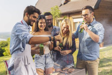 Bir grup arkadaş arka bahçede barbekü yapıyor, bira içiyor ve güneşli bir yaz gününde eğleniyorlar.