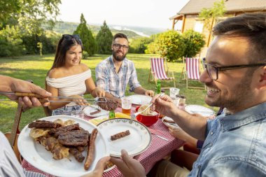 Bir grup arkadaş dışarıda barbekü yapıyor, ızgara et yiyor, bira içiyor ve eğleniyorlar. Ete odaklan.