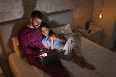 Güzel bir çift gece yatakta yatar, dizüstü bilgisayar kullanır ve yoğun bir günün ardından evde dinlenir.