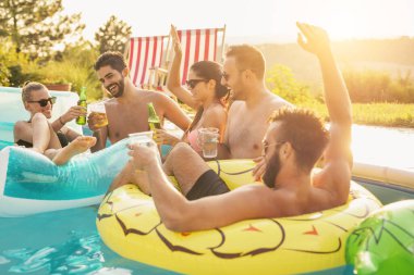 Havuz başında bir yaz partisinde bir grup arkadaş, yüzme havuzunda eğleniyorlar, kokteyl ve bira içiyorlar ve kadeh kaldırıyorlar.