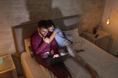 Güzel bir çift gece yatakta yatar, dizüstü bilgisayar kullanır ve yoğun bir günün ardından evde dinlenir.