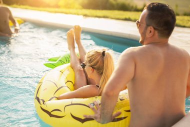 Havuz başında bir yaz partisinde aşık bir çift, güneşleniyor ve eğleniyor; kız ananas şeklinde bir şişme yatakta havuzda yüzüyor. 