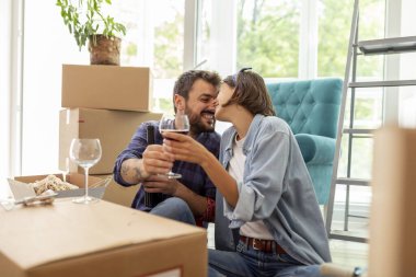 Yeni bir daireye taşınıp şarap içip öpüşmeyi kutlayan güzel, genç bir çift.