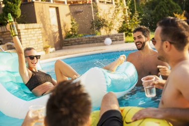 Havuz başında bir yaz partisinde bir grup arkadaş, yüzme havuzunda eğleniyorlar, kokteyl ve bira içiyorlar ve kadeh kaldırıyorlar.