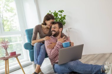 Birbirini seven bir çift evde dinleniyor, sarılıyor, kahve içiyor ve internette dizüstü bilgisayarda sörf yapıyor.