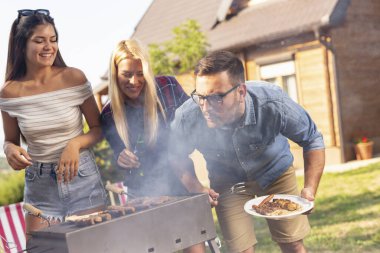 Bir grup arkadaş arka bahçede barbekü yapıyor ve güneşli bir yaz gününde eğleniyorlar. Adama odaklan.