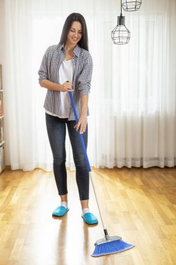 Kadın ev işi yapıyor, süpürge tutuyor ve yerleri süpürüyor.