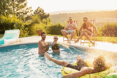 Havuz başında bir yaz partisinde bir grup arkadaş yüzme havuzunda eğleniyor, bira içiyor ve su sıçratıyor.