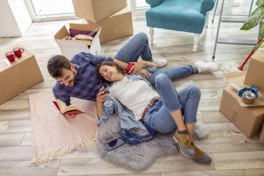 Yeni evlerine taşınan, dinlenen, yerde uzanan, şarap içen ve kitap okuyan çiftin yüksek açılı görüntüsü.