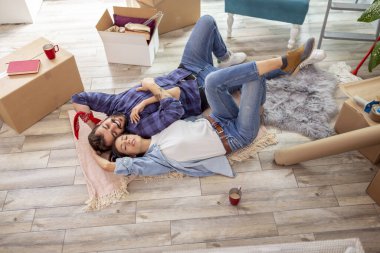 Yeni evlerinin zemininde yatan ve birlikte yaşamaya devam ederken dinlenen güzel genç çiftin yüksek açılı görüntüsü.