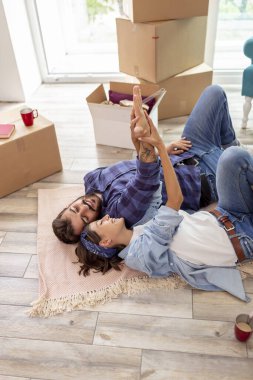 Yeni evlerinin zemininde yatan ve birlikte yaşamaya devam ederken dinlenen güzel genç çiftin yüksek açılı görüntüsü.