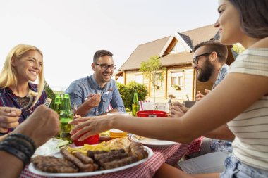 Bir grup arkadaş dışarıda barbekü yapıyor, ızgara et yiyor, bira içiyor ve eğleniyorlar. Ortadaki adama odaklan.