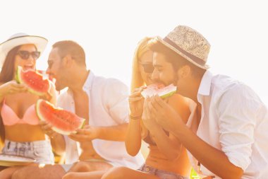 Havuz başında bir yaz partisinde bir grup arkadaş, yüzme havuzunun kenarında oturmuş, soğuk karpuz dilimleri yiyor ve eğleniyorlar.